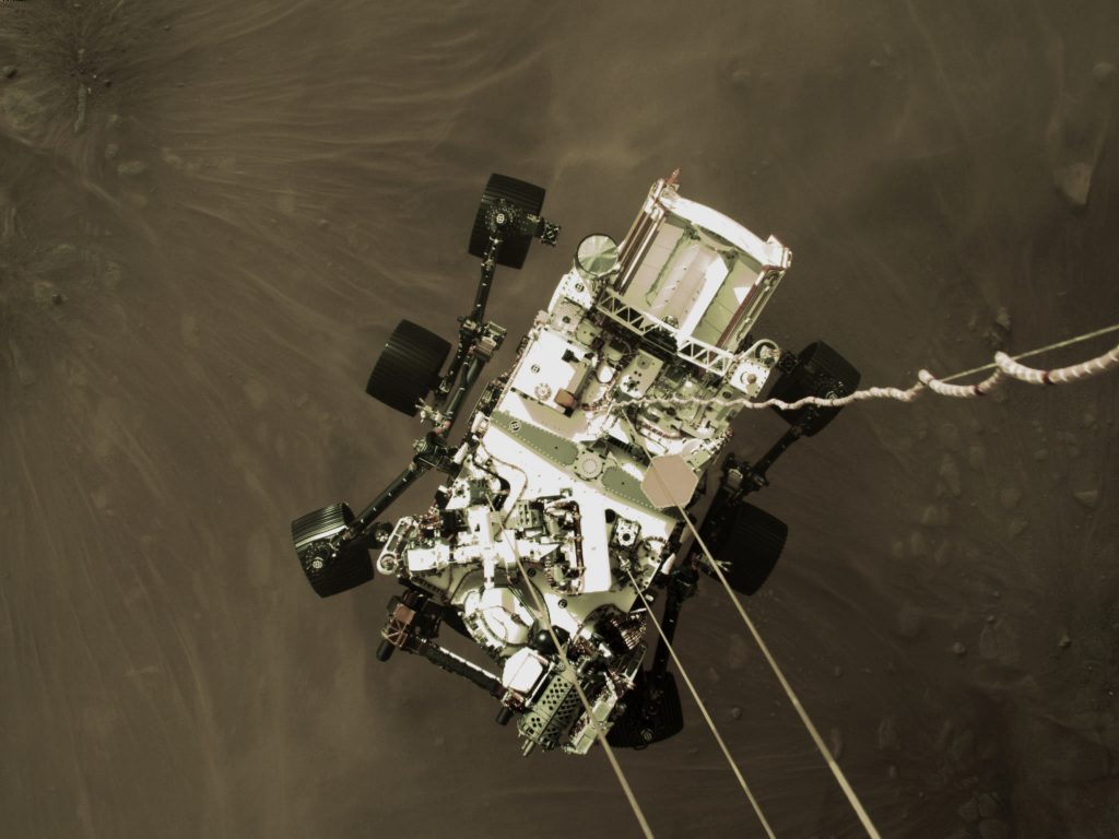The car-sized Perseverance rover, suspended by tethers from its powered descent stage, a couple of meters above the surface, just seconds before touchdown, on Mars