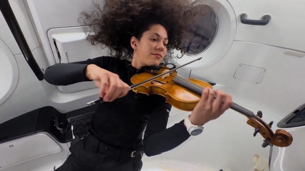 Sarah Gillis playing violin in Dragon spacecraft